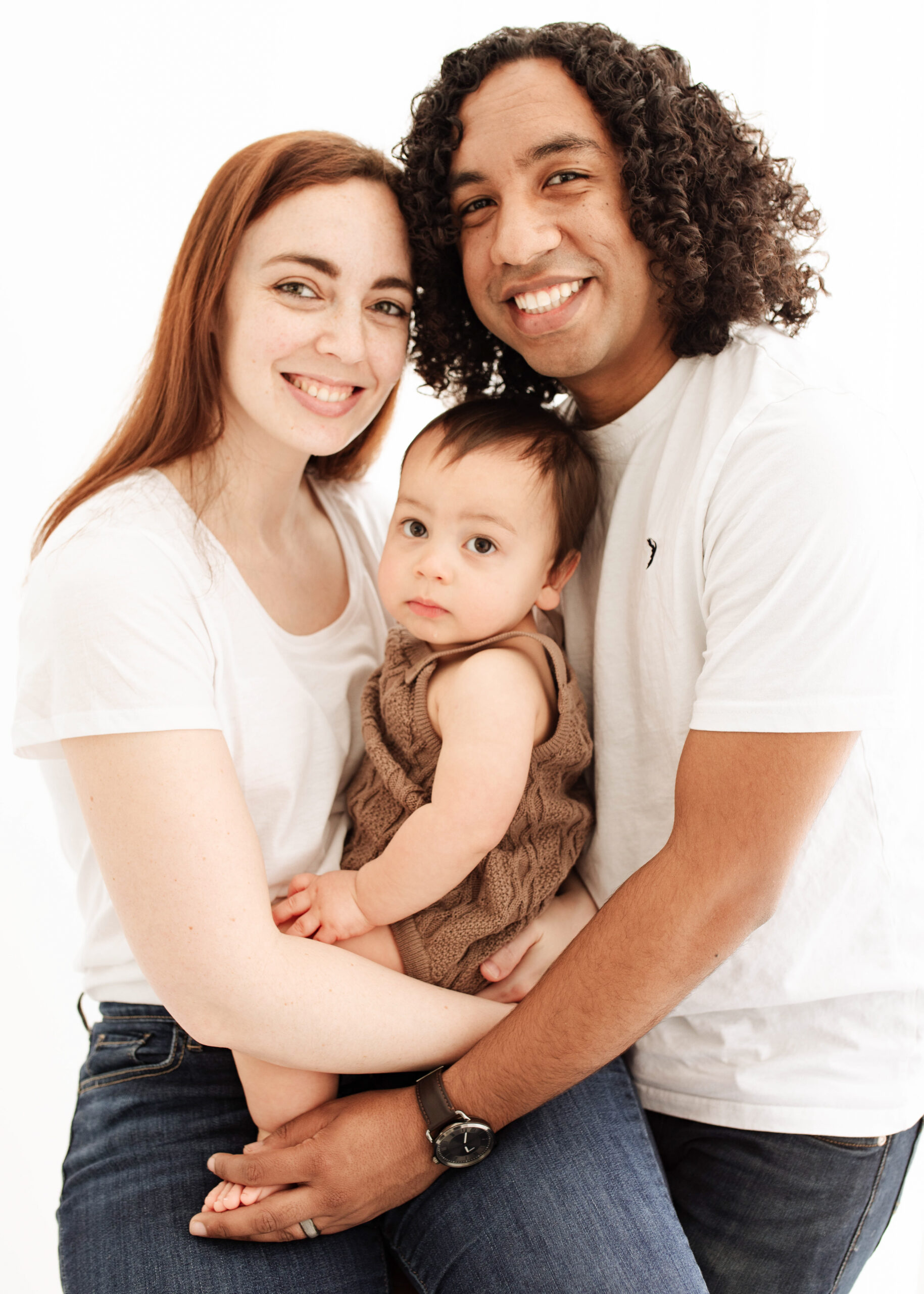 a family of mum, dad and baby at the photoshoot smiling into the camera